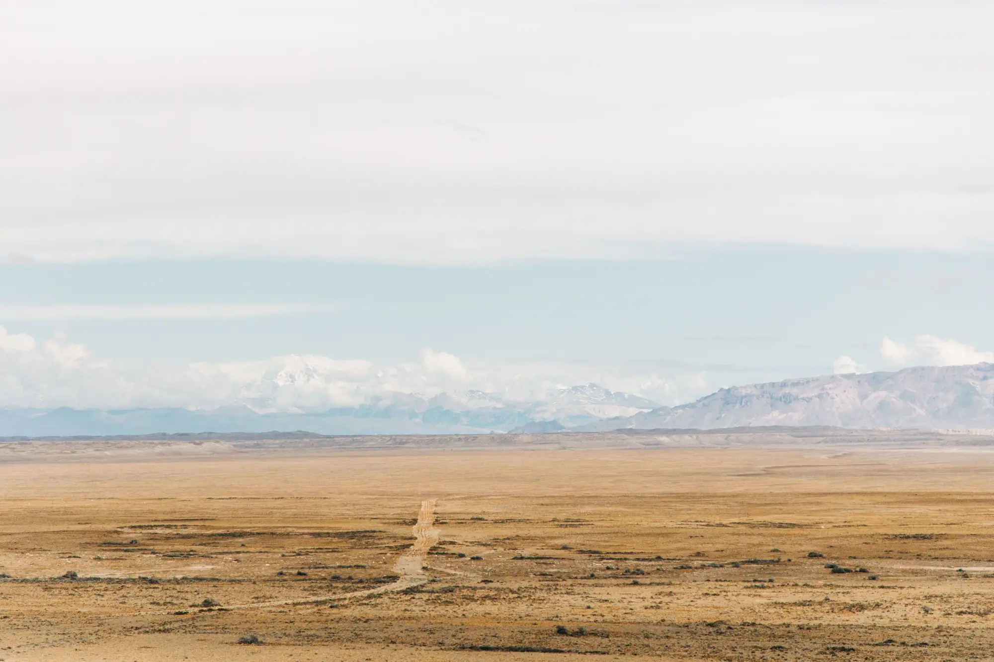 A dry plain running flat to a far mountain range, one dirt track crossing it